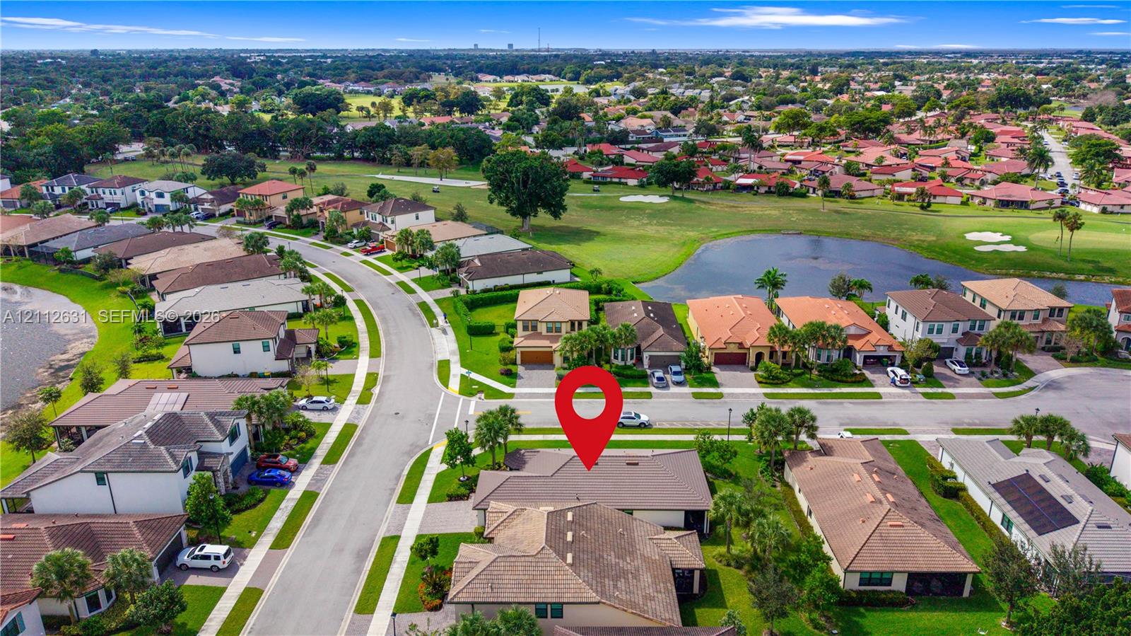 Aerial perspective featuring a multi-hipped shingle roof, paver driveway, and landscaped front lawn situated within a residential community
