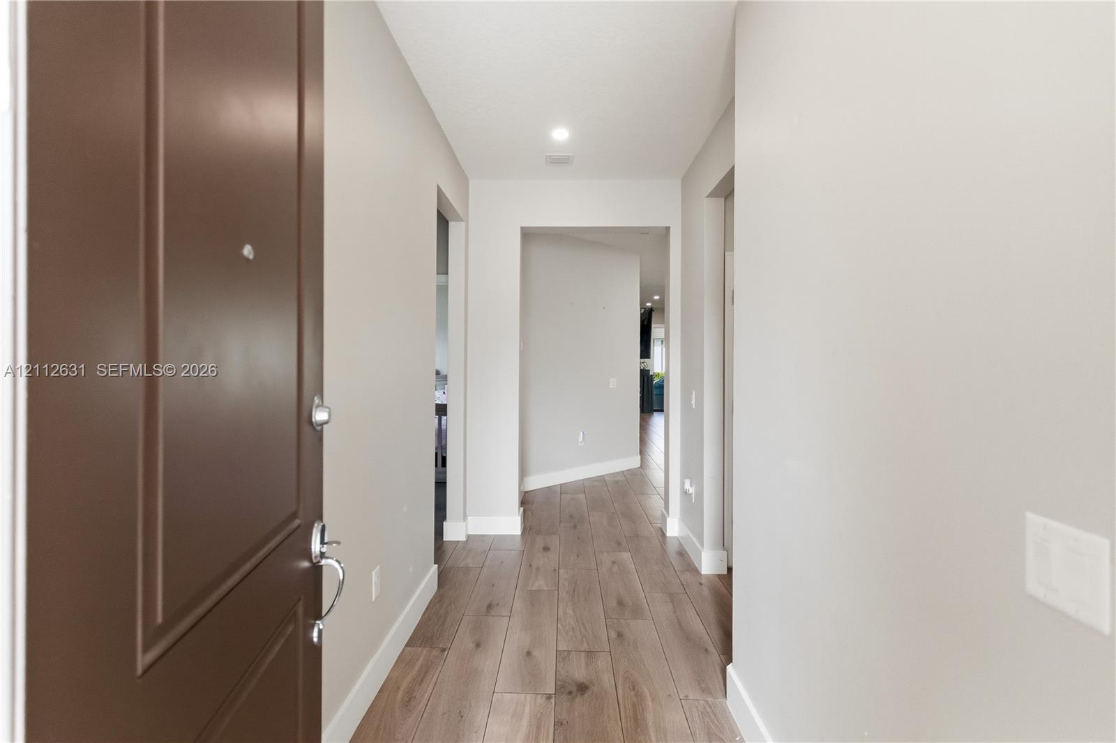 Entry foyer featuring wood-finish flooring, a solid-panel door with metallic hardware, neutral wall paint, and recessed ceiling lighting Entry foyer featuring wood-finish flooring, a solid-panel door with metallic hardware, neutral wall paint, and recessed ceiling lighting