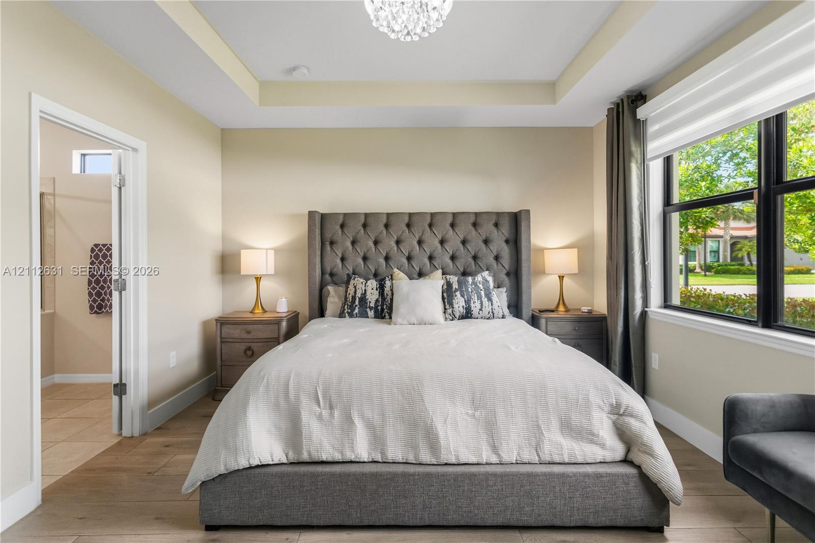 Tray ceiling featuring a central chandelier, wood-finish flooring, and black-trimmed windows