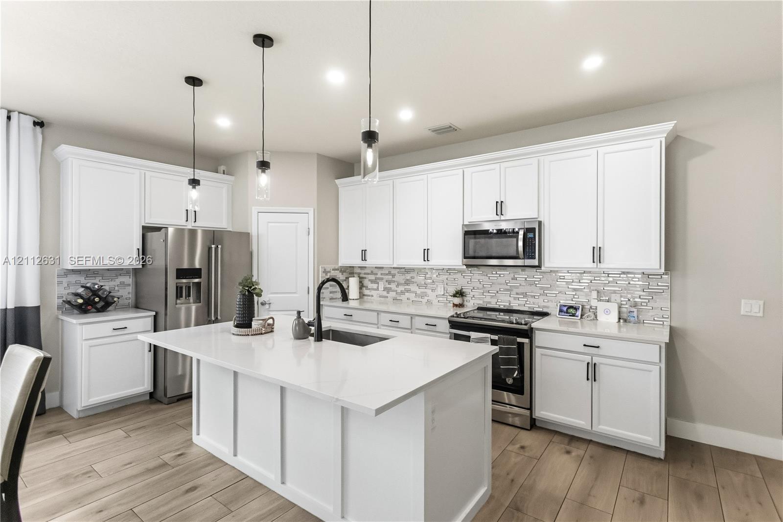 Kitchen featuring white cabinetry, quartz countertops, a central island with a sink, stainless steel appliances, and wood-finish flooring