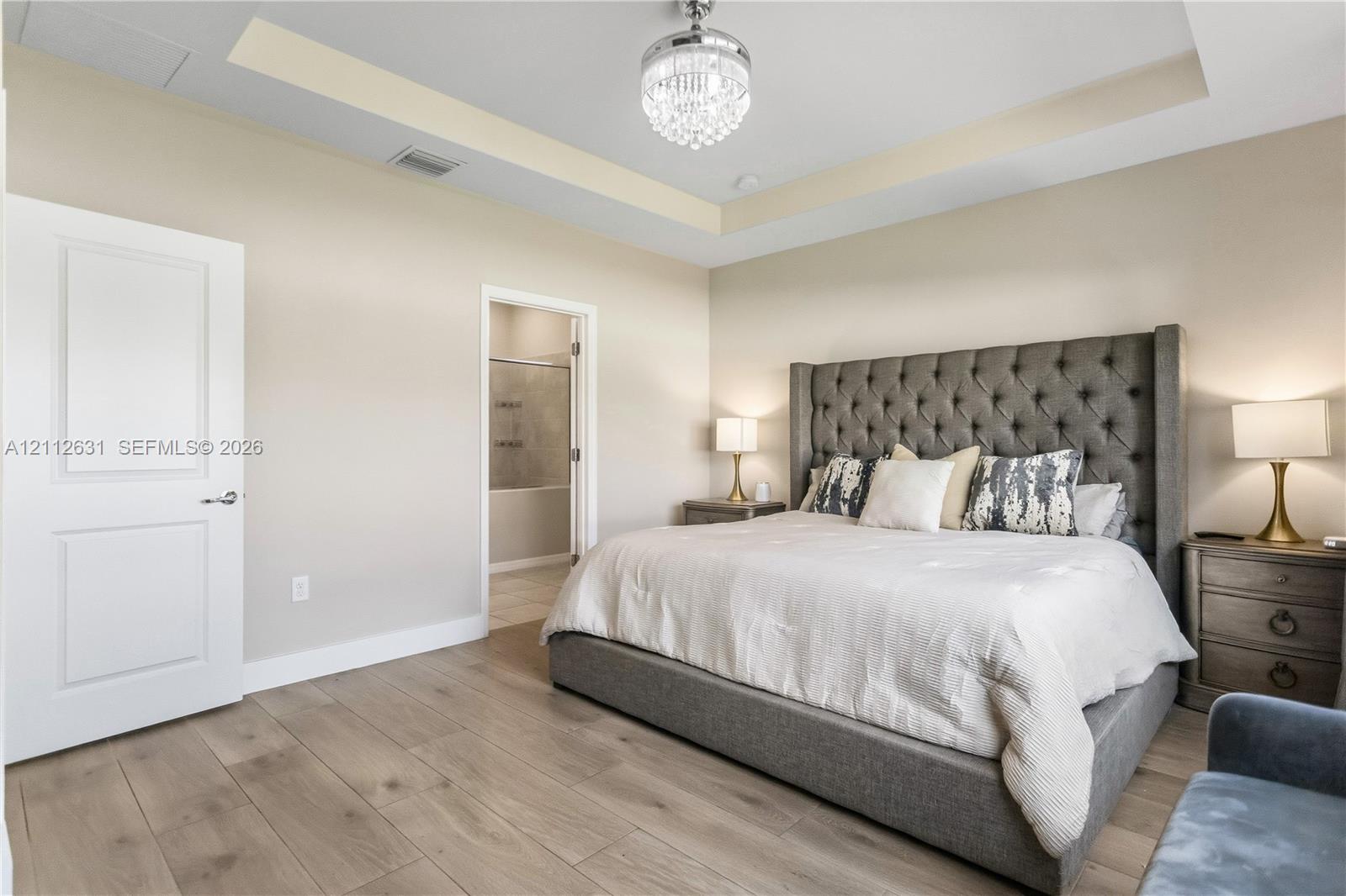 Tray ceiling featuring a recessed design, wood-finish flooring, and a decorative crystal chandelier