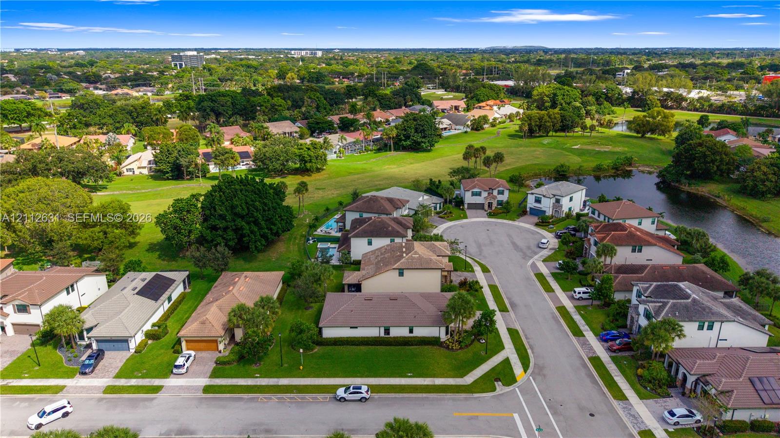 Aerial perspective of a residential community featuring expansive green spaces, manicured landscaping, a winding water feature, and paved cul-de-sac streets