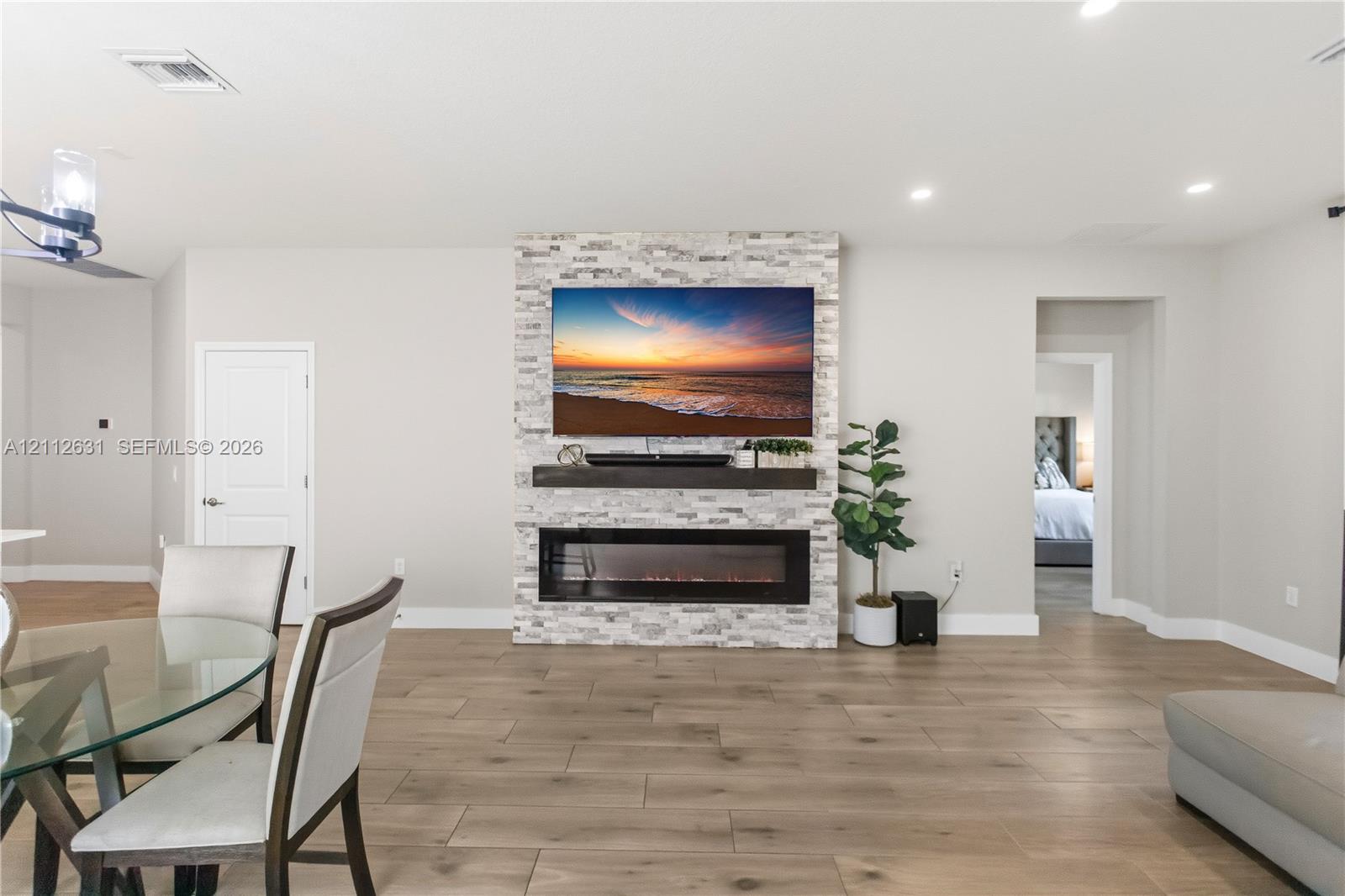 Floor-to-ceiling stone veneer fireplace surround with a linear electric hearth, wood-finish flooring, and recessed ceiling lighting
