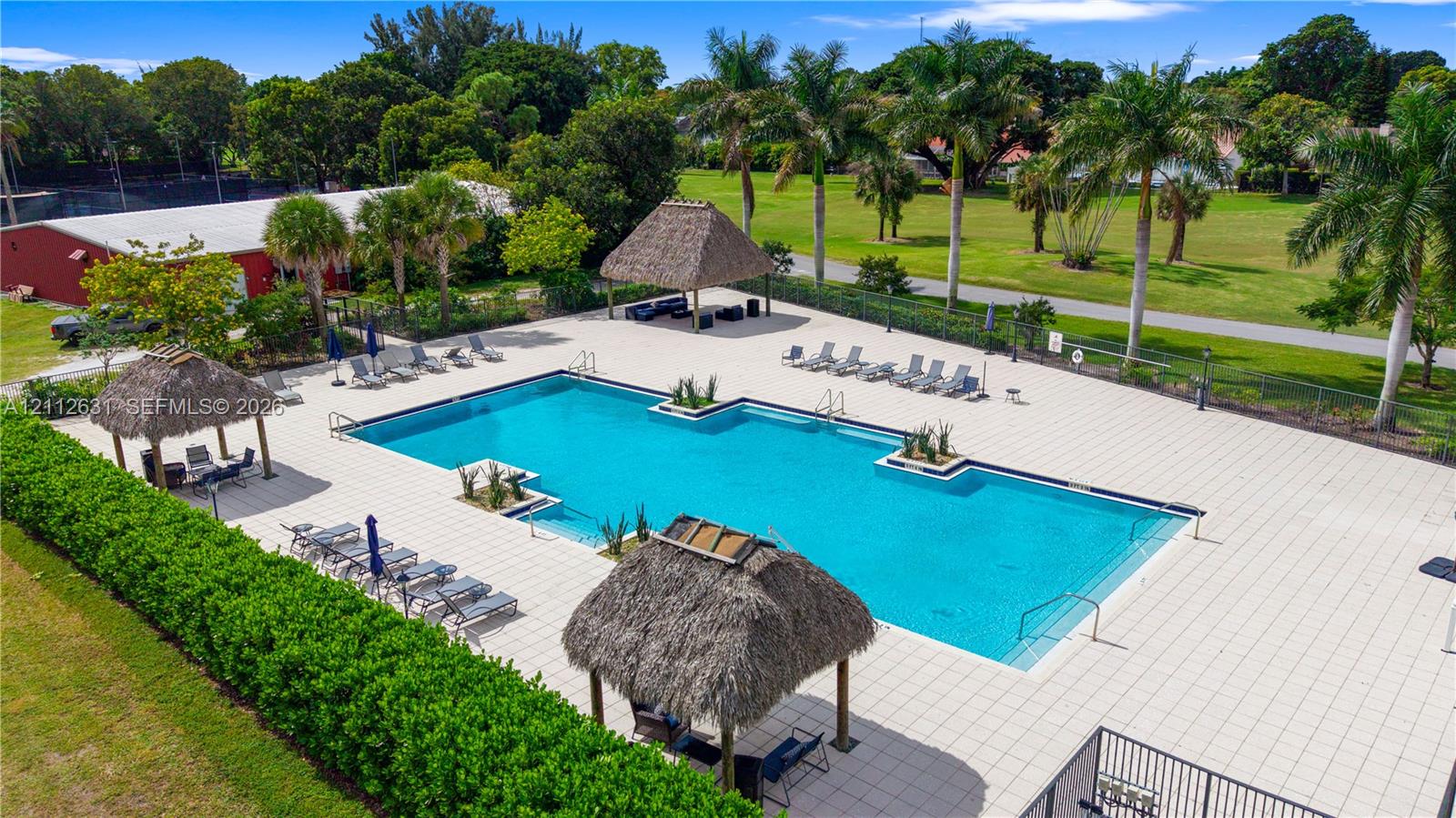 In-ground swimming pool featuring a large concrete deck, integrated planters, and multiple thatched-roof cabanas