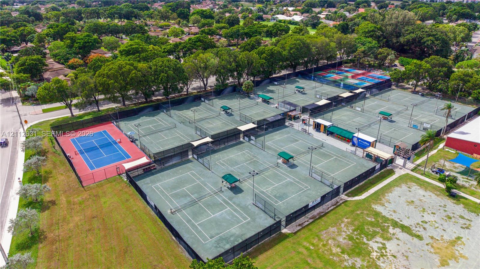 Multi-court tennis facility featuring high-fencing enclosures, integrated court lighting, paved walkways, and shade structures
