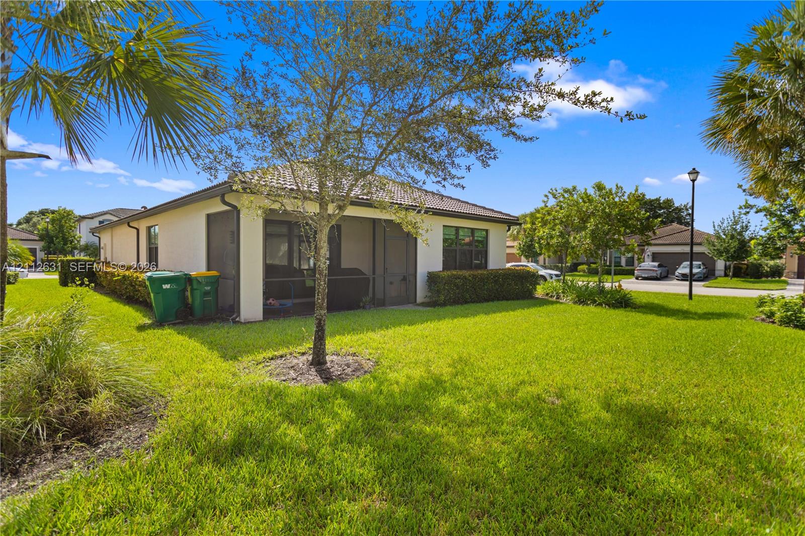 Stucco exterior featuring a tiled roof, screened-in porch, mature landscaping, and an expansive lawn Stucco exterior featuring a tiled roof, screened-in porch, mature landscaping, and an expansive lawn