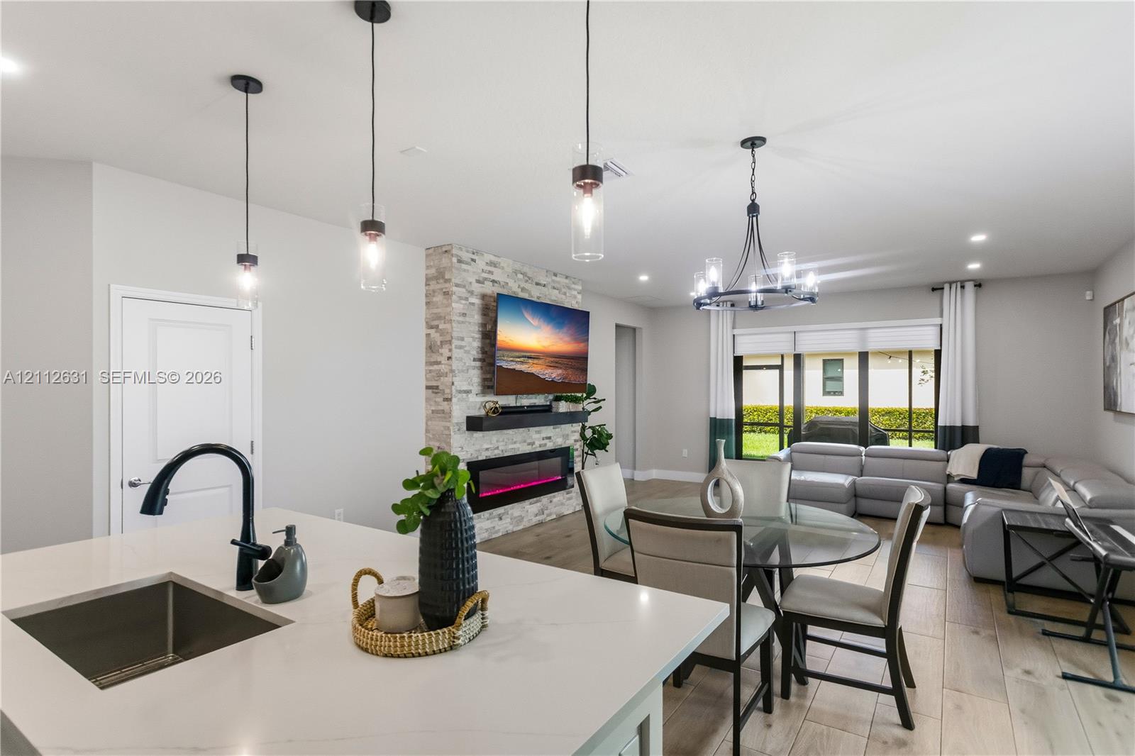 Open-concept space featuring wood-finish flooring, a kitchen island with a quartz countertop, a matte black faucet, and a floor-to-ceiling stone-clad fireplace with an integrated electric firebox