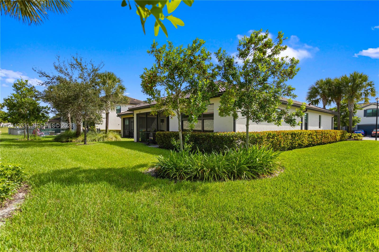 Stucco exterior featuring a screened-in lanai, mature landscaping, manicured lawn, and multi-pitched roofline Stucco exterior featuring a screened-in lanai, mature landscaping, manicured lawn, and multi-pitched roofline