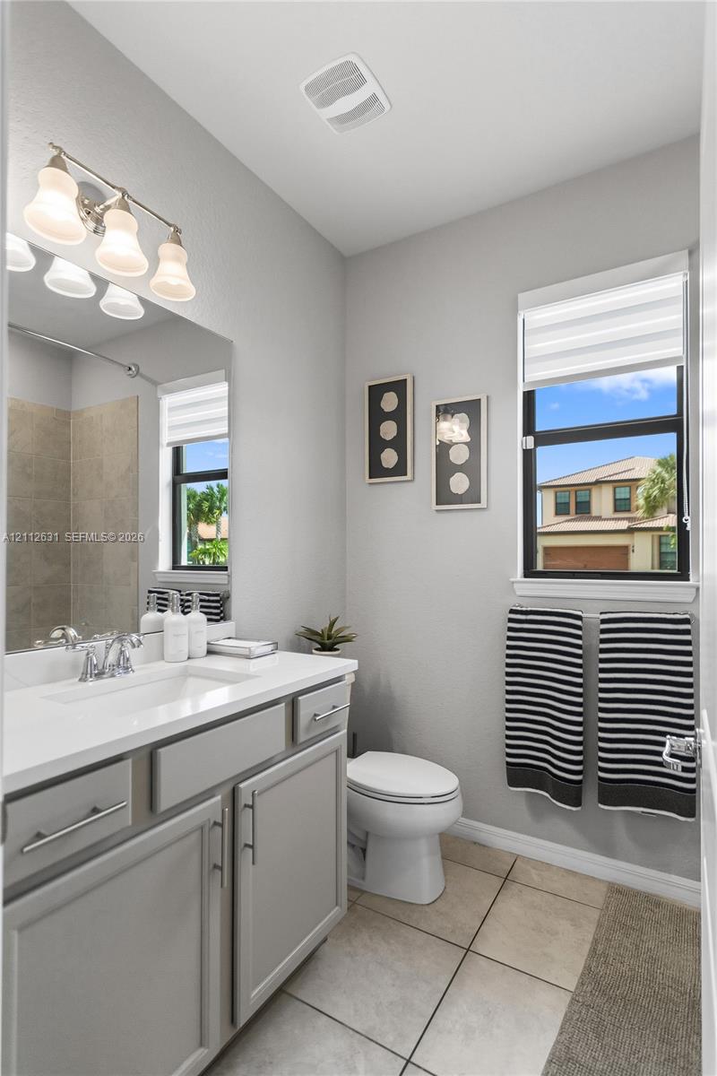 Bathroom featuring a white countertop vanity with gray cabinetry, a wall-to-wall mirror, a three-light fixture, and ceramic tile flooring