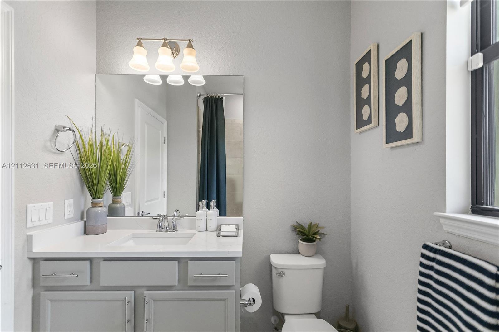 Bathroom featuring a light-toned vanity with a rectangular undermount sink, solid surface countertop, polished chrome fixtures, and a triple-light wall-mounted fixture above a rectangular mirror