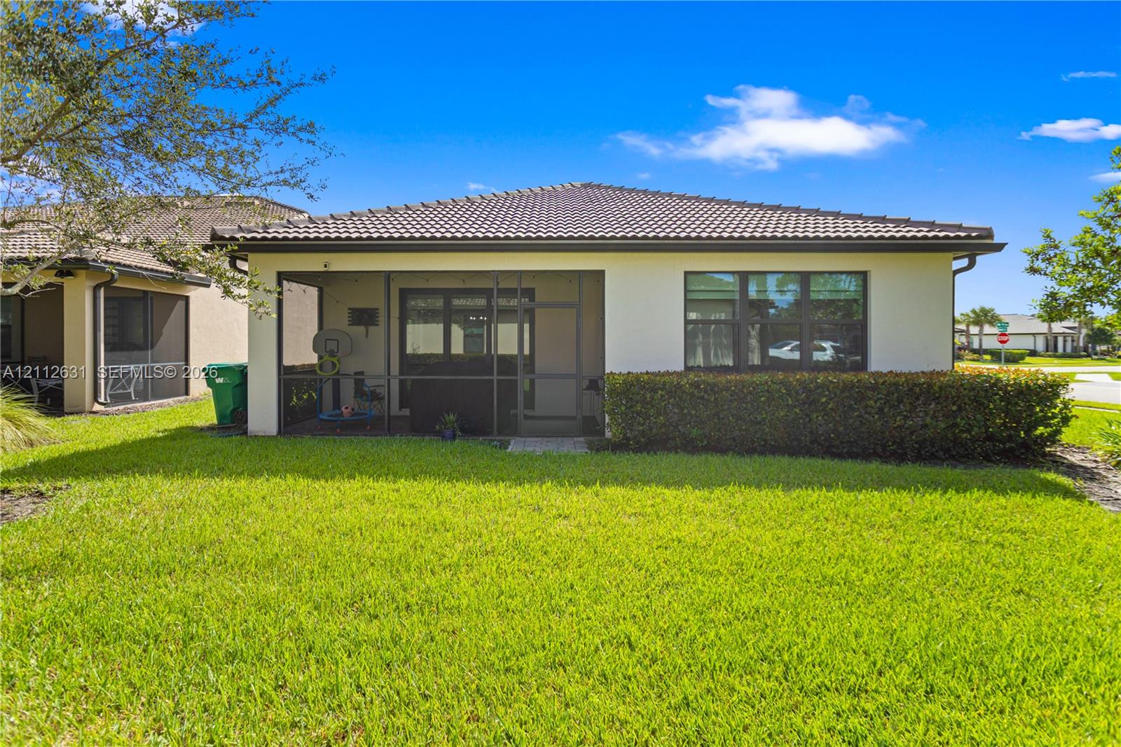 Exterior rear elevation featuring a screened-in lanai, stucco facade, tiled roof, and manicured lawn Exterior rear elevation featuring a screened-in lanai, stucco facade, tiled roof, and manicured lawn