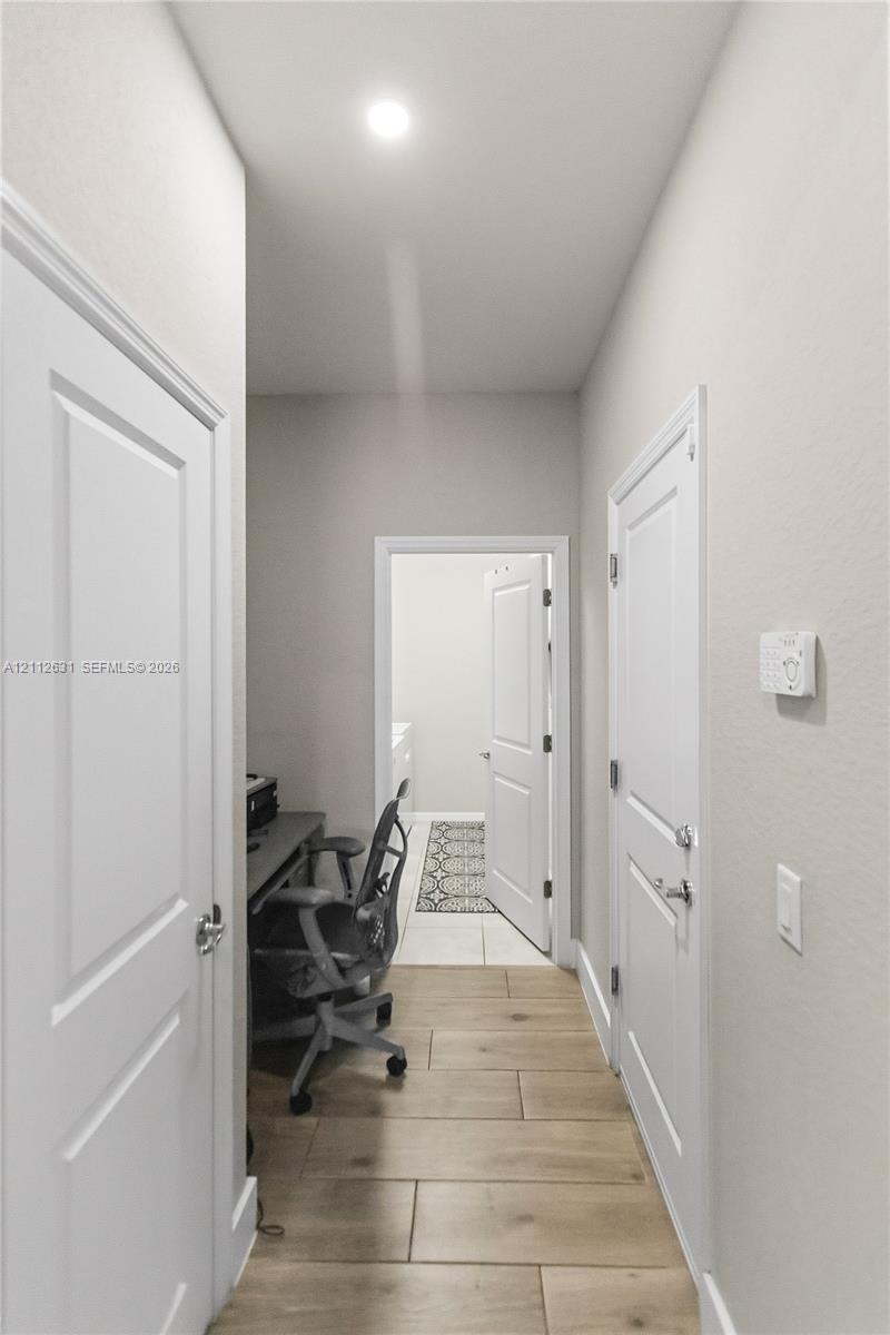 Hallway featuring wood-finish tile flooring, recessed ceiling lighting, and multiple two-panel interior doors