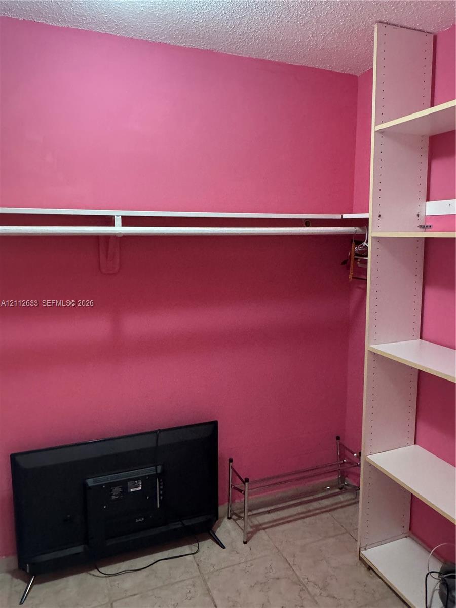 Storage area featuring built-in vertical shelving, a horizontal clothes rod, and tile flooring