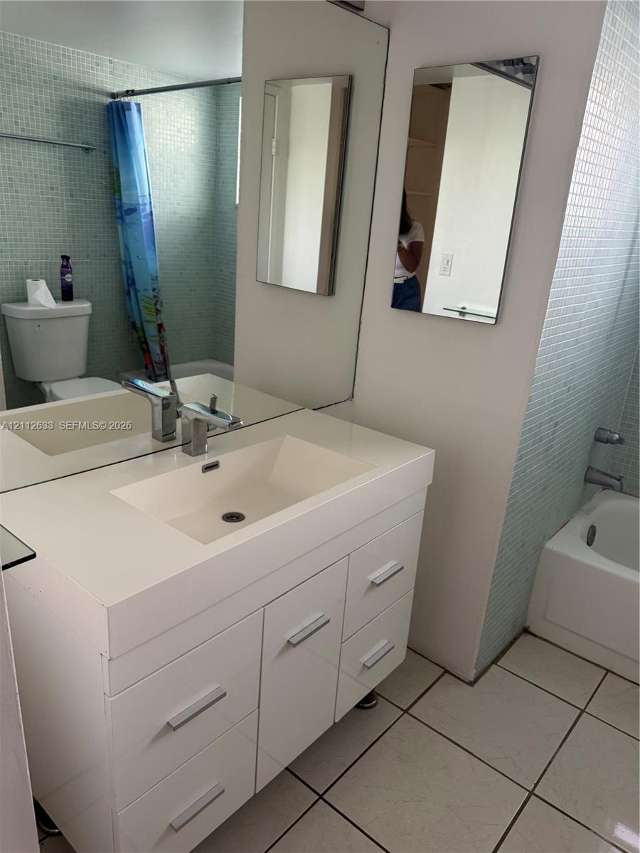 Bathroom featuring a white vanity with an integrated sink, brushed metal hardware, a large wall-mounted mirror, light-toned mosaic wall tile, and white floor tile