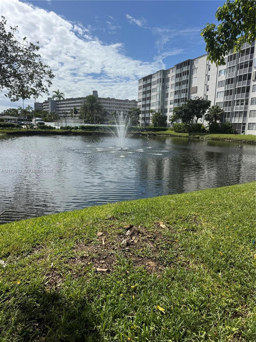 Water feature with a central fountain situated within a community pond, surrounded by landscaped lawn and mature trees