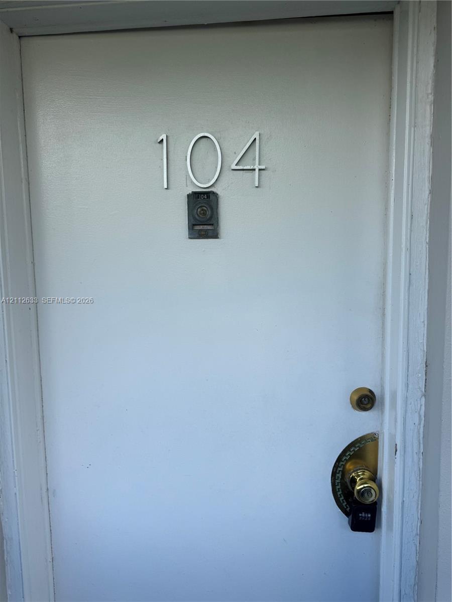 Solid door entry featuring metallic house numbering, a peephole, and a brass-tone lever handle set