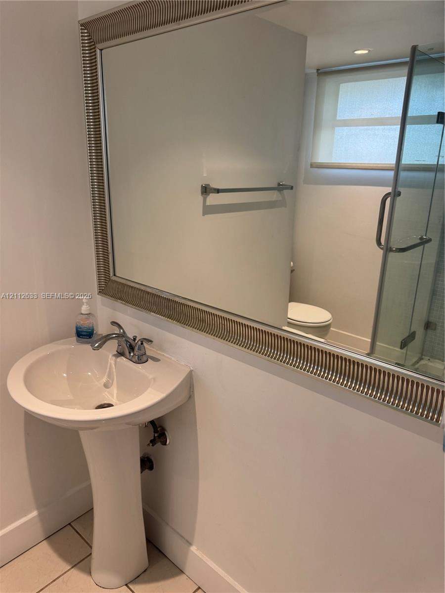 Pedestal sink with polished chrome double-handle faucet, large decorative framed mirror, glass-enclosed shower, and light-toned tile flooring