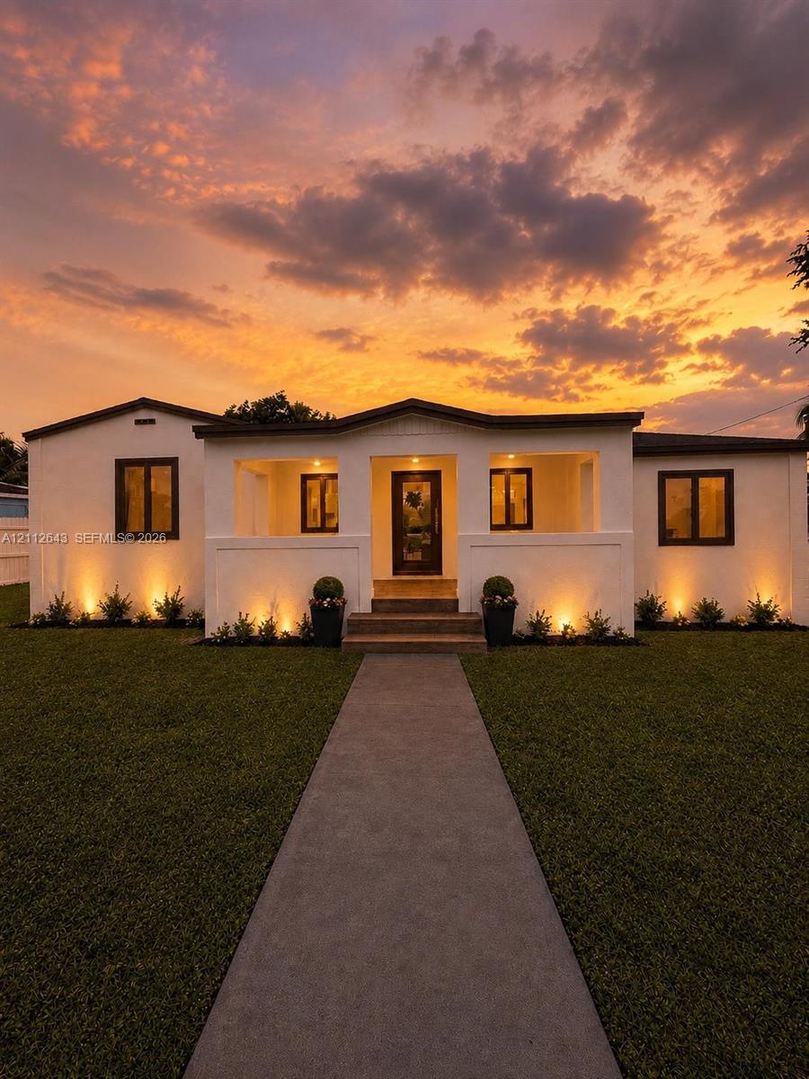 Stucco exterior featuring a covered front porch, concrete walkway, and uniform dark-trimmed windows Stucco exterior featuring a covered front porch, concrete walkway, and uniform dark-trimmed windows