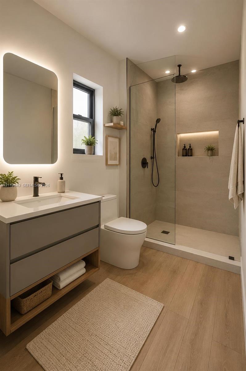 Modern bathroom featuring a gray dual-drawer floating vanity with a white countertop, backlit mirror, wood-finish flooring, and a walk-in shower with a glass enclosure, matte black rainfall showerhead, and integrated recessed shelving Modern bathroom featuring a gray dual-drawer floating vanity with a white countertop, backlit mirror, wood-finish flooring, and a walk-in shower with a glass enclosure, matte black rainfall showerhead, and integrated recessed shelving