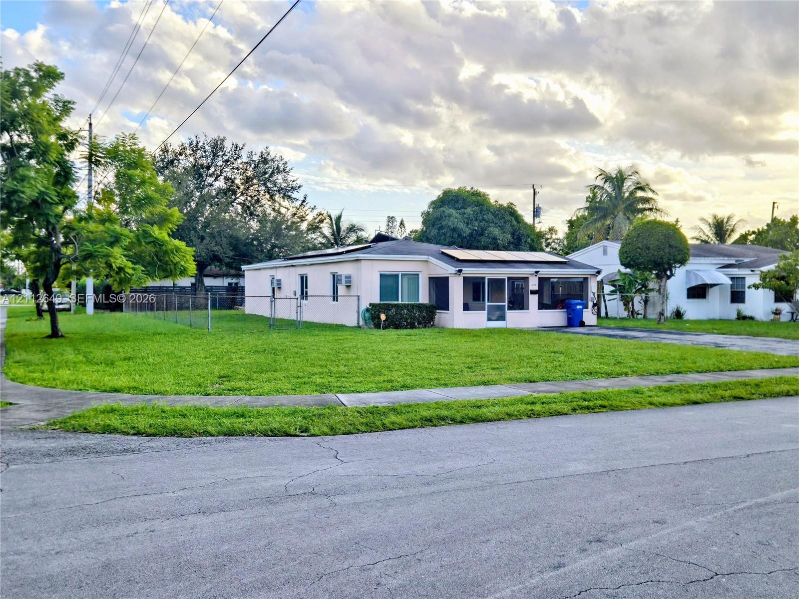 Single-story residence featuring a smooth stucco exterior, integrated rooftop solar panels, a screened-in porch, and a chain-link fenced yard Single-story residence featuring a smooth stucco exterior, integrated rooftop solar panels, a screened-in porch, and a chain-link fenced yard