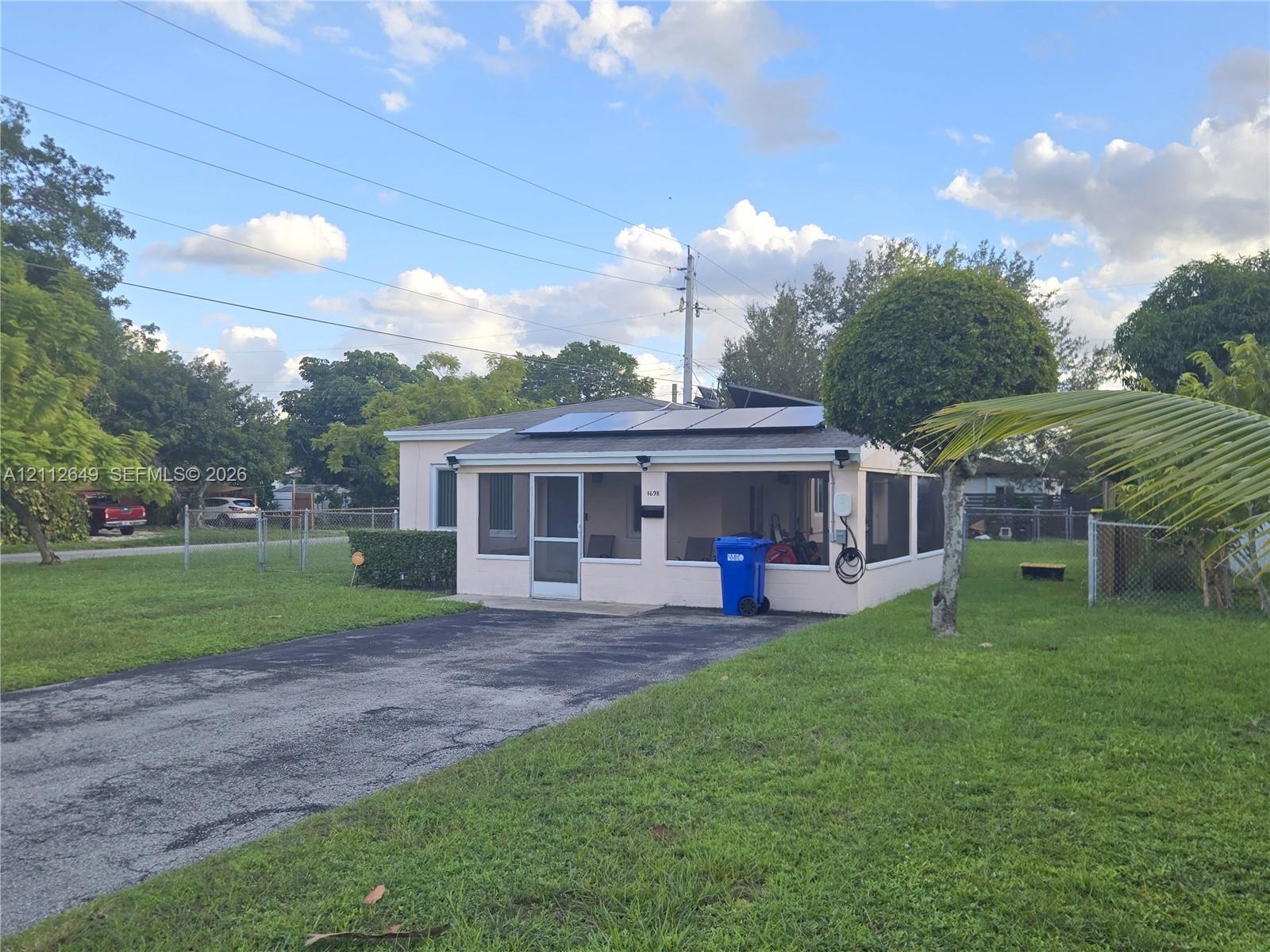 Single-story exterior featuring a screened-in porch, roof-mounted solar panels, asphalt driveway, and expansive lawn Single-story exterior featuring a screened-in porch, roof-mounted solar panels, asphalt driveway, and expansive lawn