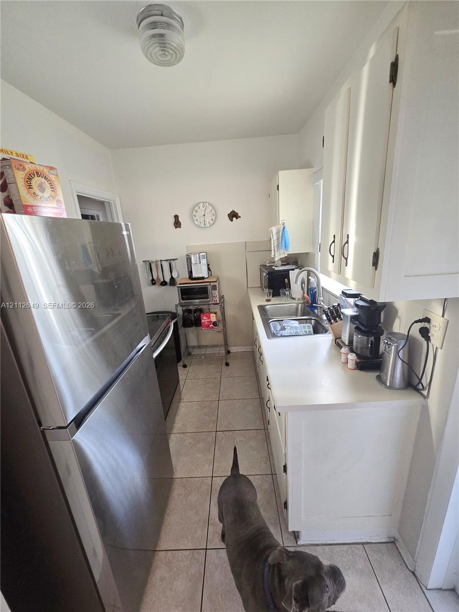 Kitchen featuring white cabinetry, stainless steel refrigerator, stainless steel sink with a high-arch faucet, and tile flooring Kitchen featuring white cabinetry, stainless steel refrigerator, stainless steel sink with a high-arch faucet, and tile flooring