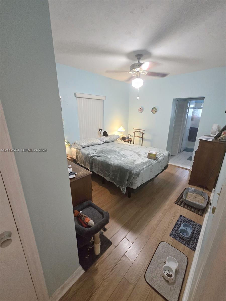 Bedroom featuring wood-finish flooring, vertical blinds, and a ceiling fan with light fixture Bedroom featuring wood-finish flooring, vertical blinds, and a ceiling fan with light fixture