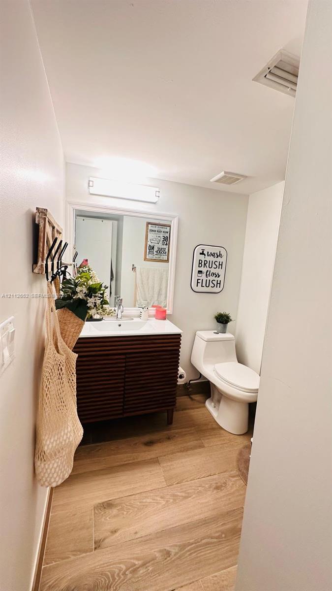 Bathroom featuring a ribbed wood-finish vanity, integrated sink basin, white-framed wall mirror, wall-mounted light fixture, and wood-finish flooring