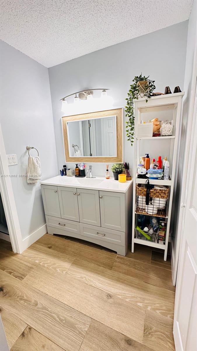 Bathroom vanity with a stone countertop, integrated undermount sink, multi-drawer cabinetry, wood-finish flooring, and a framed mirror