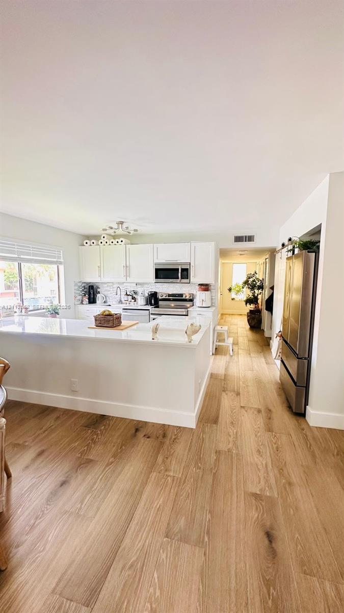 Kitchen featuring white cabinetry, solid-surface countertops, wood-finish flooring, and stainless steel appliances