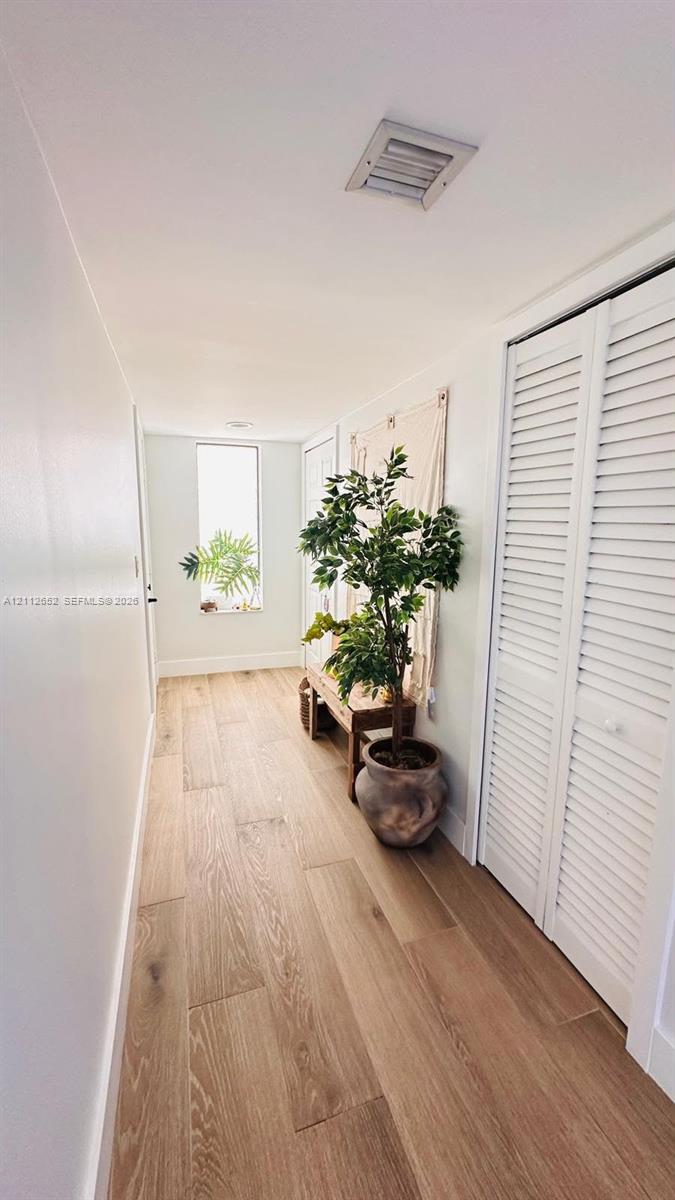 Hallway featuring wood-finish flooring, white louvered closet doors, and an elongated rectangular window