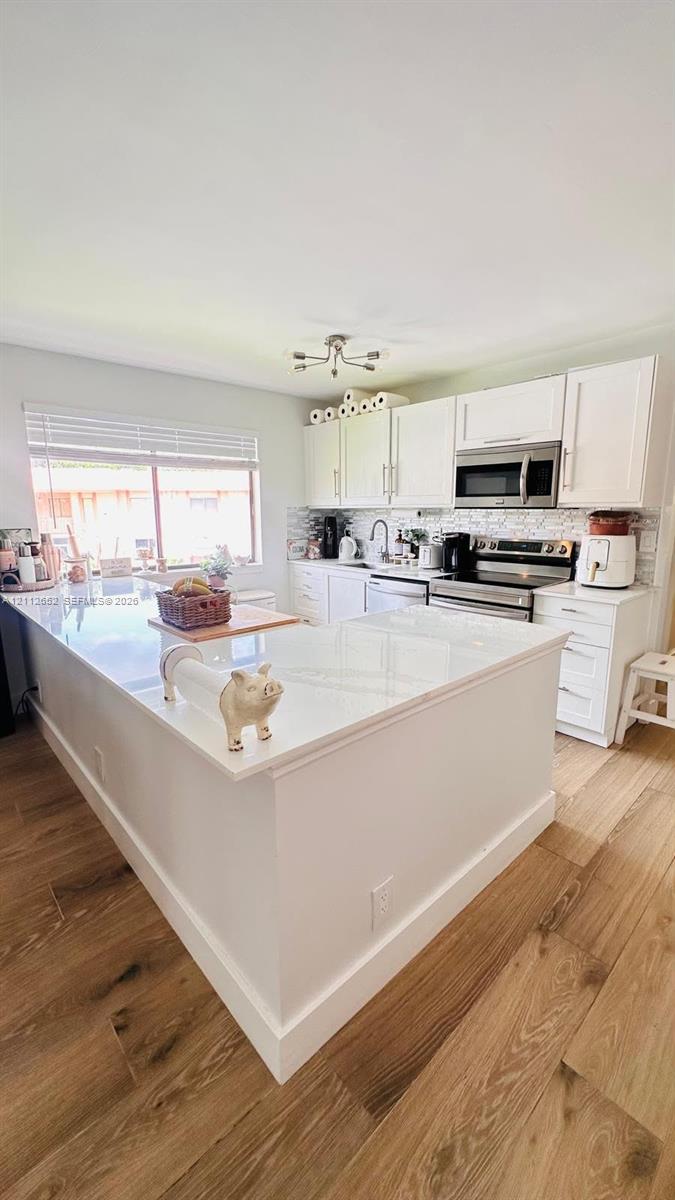 Kitchen featuring white cabinetry, solid-surface countertops, wood-finish flooring, a multi-light ceiling fixture, and stainless steel built-in appliances