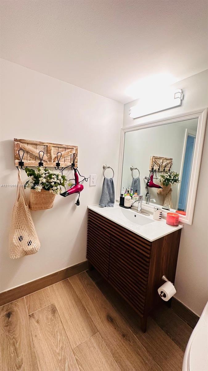Slatted-wood vanity featuring a rectangular integrated sink, white countertop, oversized framed wall mirror, and wood-finish flooring