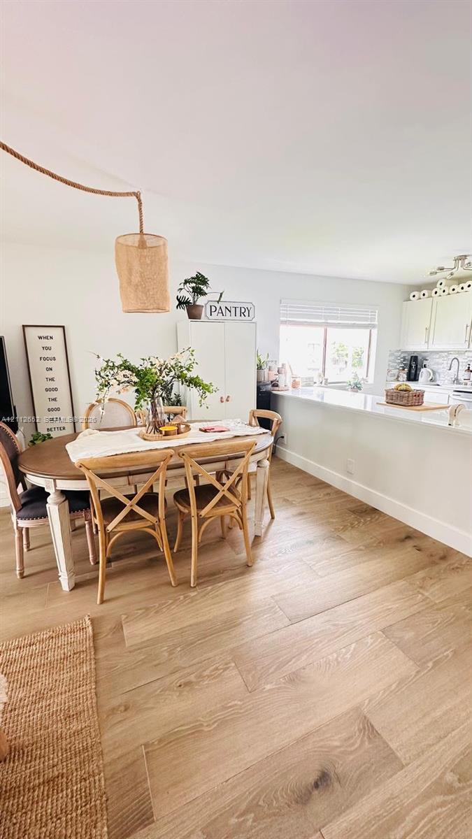 Dining area featuring wood-finish flooring, a suspended woven pendant light, and a peninsula with a stone countertop