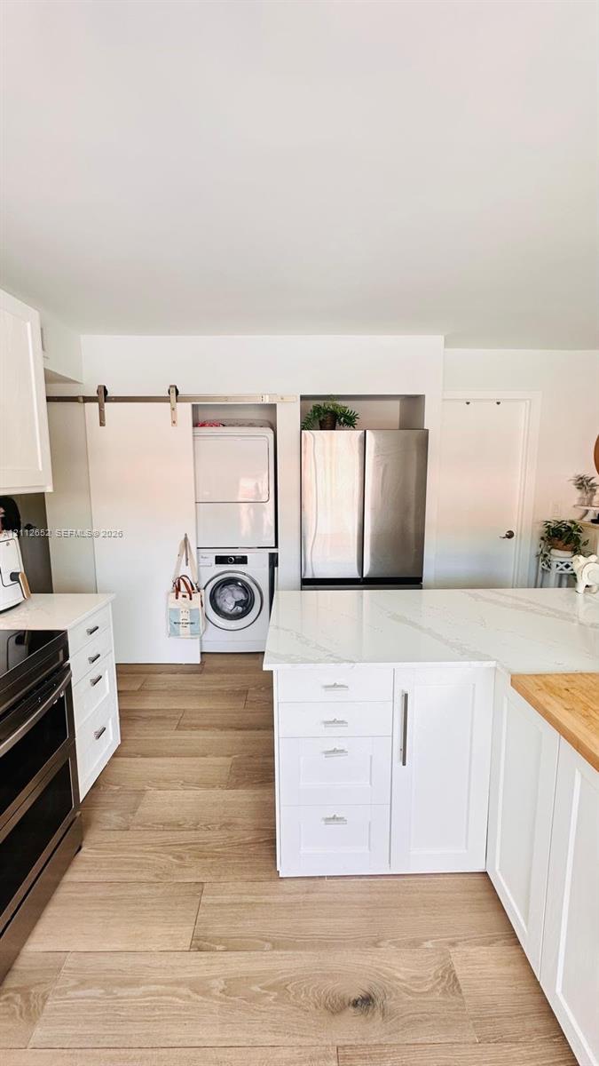 Kitchen featuring white cabinetry, wood-finish flooring, stone-surfaced countertops, a stainless steel refrigerator, and a sliding barn door concealing laundry area