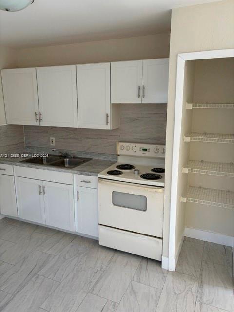 Kitchen featuring white cabinetry with metallic pulls, stone-patterned laminate countertops, integrated double-basin sink, electric range, and a built-in pantry with wire shelving