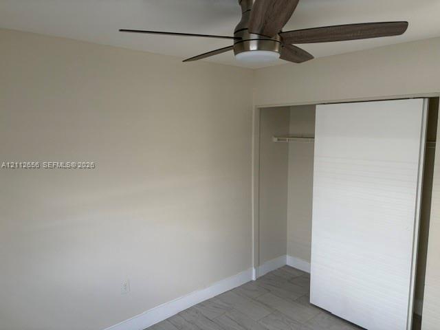 Neutral-toned walls featuring a ceiling-mounted fan with wood-finish blades and an integrated light fixture, accompanied by a closet with a horizontal-slatted sliding door and tile flooring
