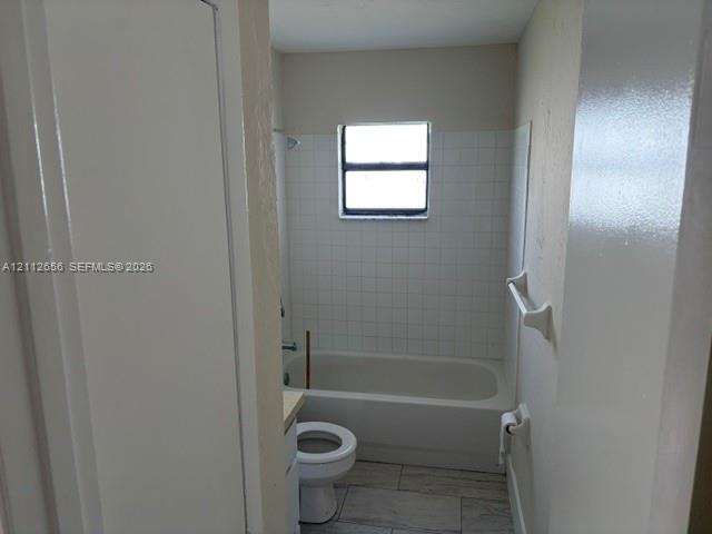 Bathroom featuring a tub-shower combination with white tile surround, a single-basin vanity, and neutral stone-finish tile flooring