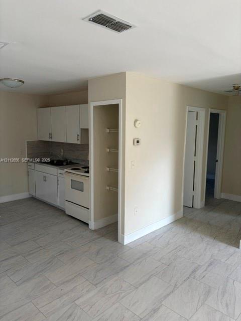 Kitchen featuring white cabinetry, stone-finish backsplash, neutral-toned tile flooring, and built-in shelving