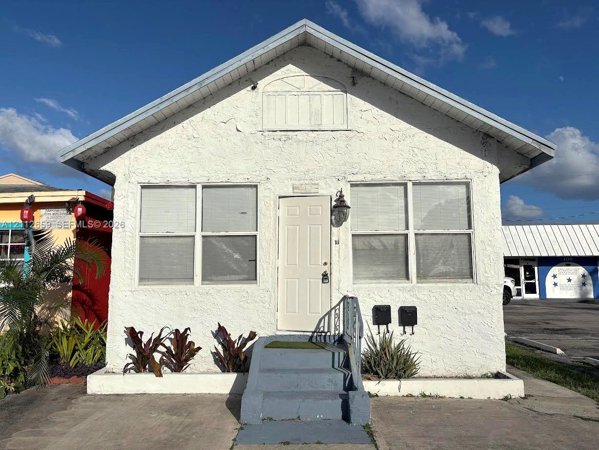 Textured stucco exterior featuring a gable roof, decorative pediment detail, exterior wall-mounted lantern lighting, and a concrete staircase with metal handrail