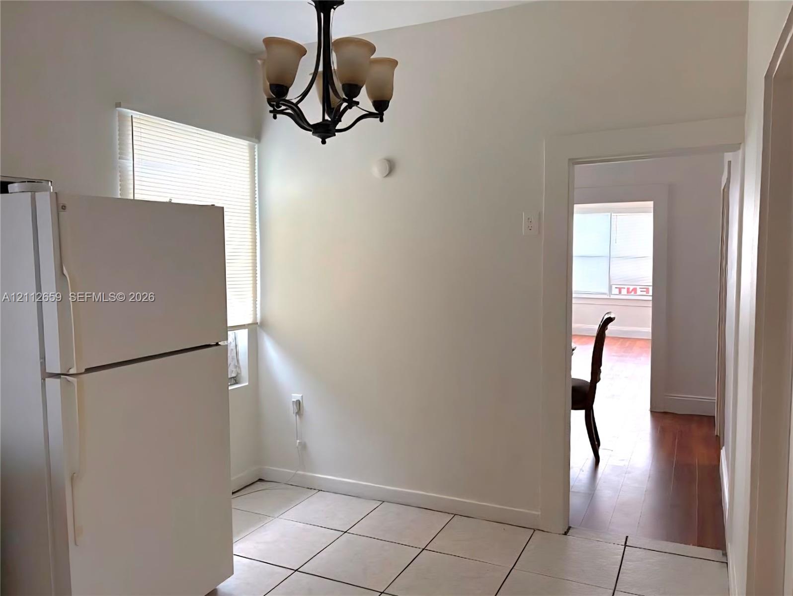 Kitchen area featuring white ceramic floor tiling, a white top-freezer refrigerator, and a dark metal four-arm chandelier with frosted glass shades Kitchen area featuring white ceramic floor tiling, a white top-freezer refrigerator, and a dark metal four-arm chandelier with frosted glass shades