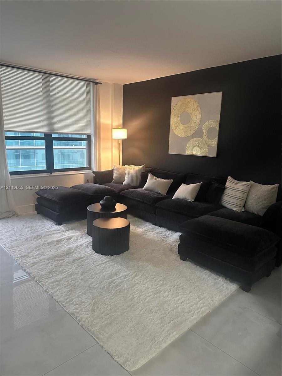 Living area featuring high-gloss tile flooring, a dark accent wall, and expansive multi-pane windows with integrated blinds