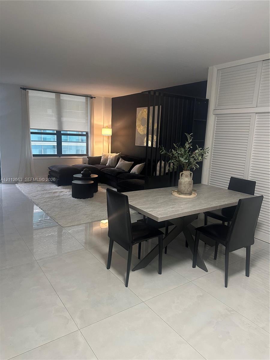 Open-concept interior featuring large-format tile flooring, a black-painted accent wall, built-in louvered-style closet doors, and expansive windows