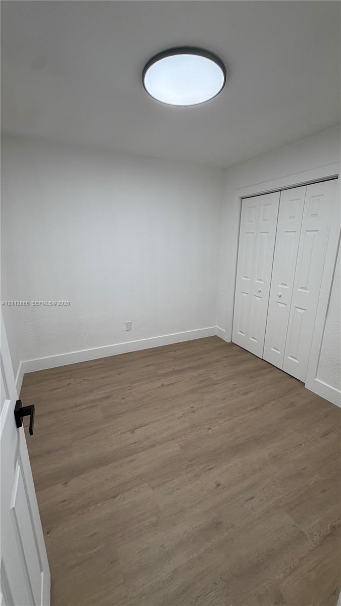 Interior space featuring wood-finish flooring, white walls, double-door closet, and flush-mount circular lighting fixture