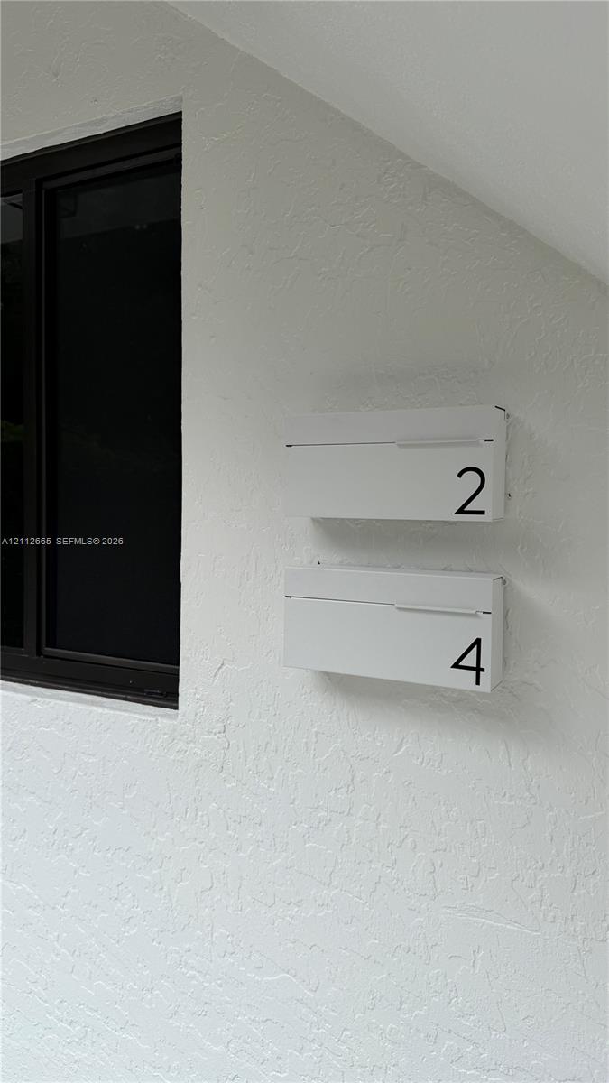 Textured white exterior wall featuring dual minimalist white mailboxes with numerical identification and a black-framed window