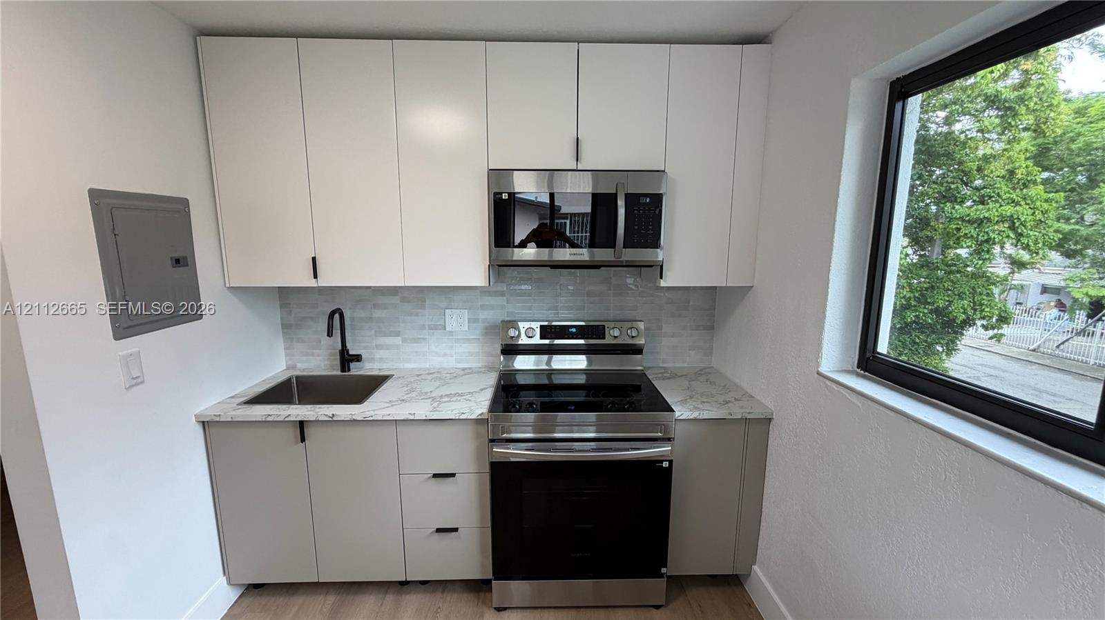 Kitchenette featuring white upper cabinetry, grey lower cabinetry, stone-patterned countertops, stainless steel appliances, and a matte black faucet Kitchenette featuring white upper cabinetry, grey lower cabinetry, stone-patterned countertops, stainless steel appliances, and a matte black faucet