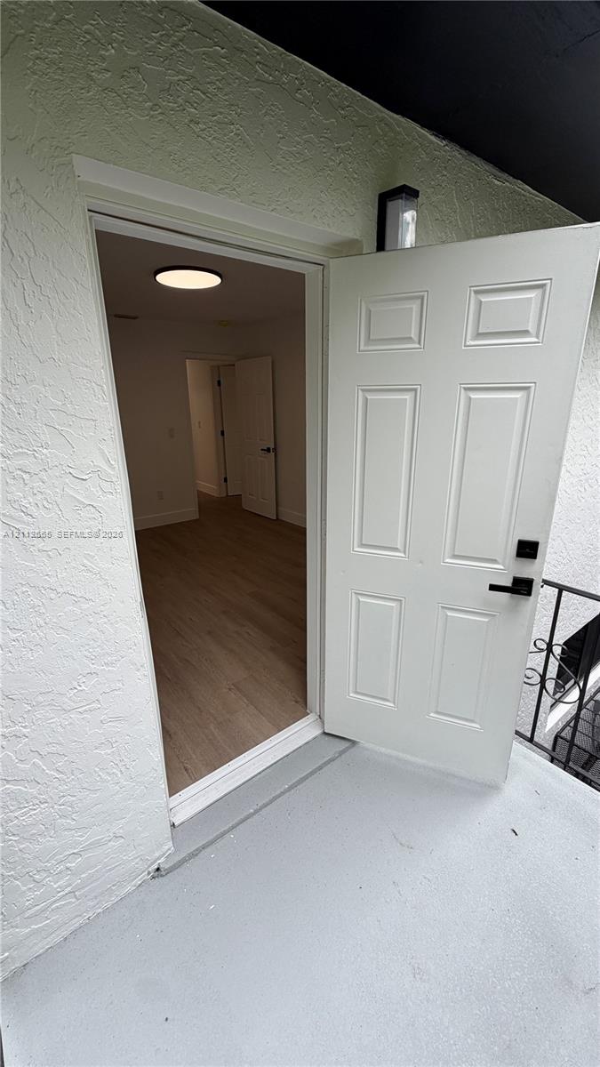 Six-panel entry door featuring a matte black electronic deadbolt and handle set, textured exterior wall finish, wood-finish flooring, and recessed circular ceiling lighting