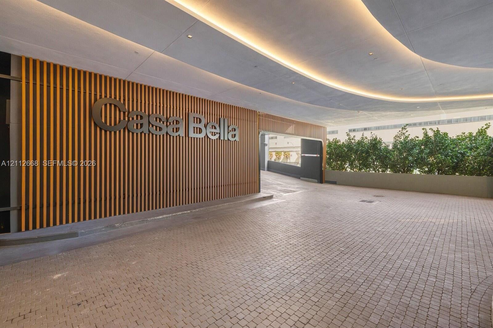 Covered arrival entrance featuring a stone paver driveway, vertical wood-slat wall accents, recessed architectural lighting, and integrated landscaping