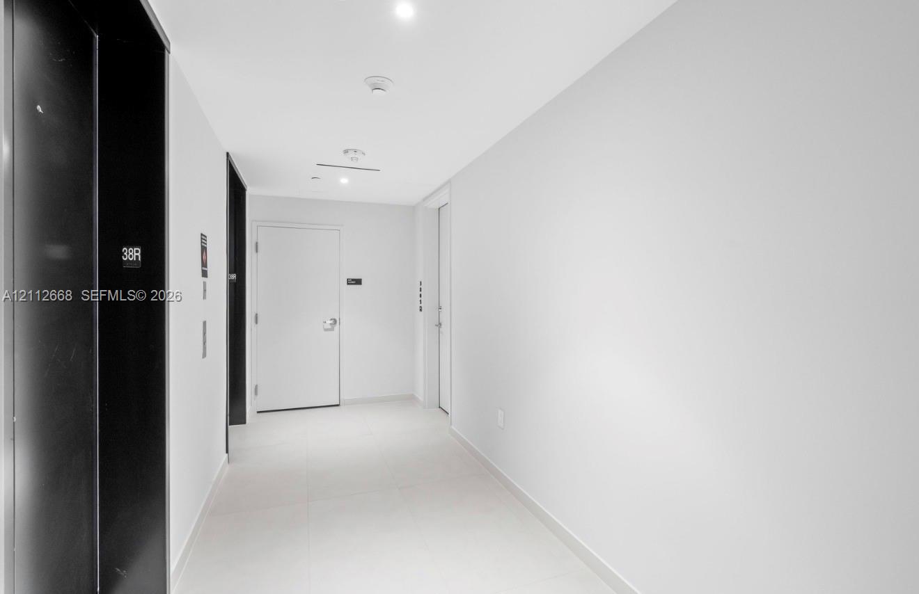 Minimalist hallway featuring white tile flooring, high-contrast black elevator doors, and recessed ceiling lighting