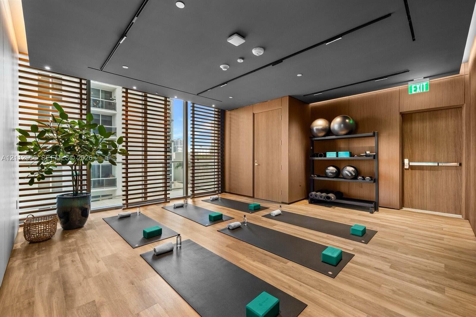 Fitness room featuring wood-finish flooring, wood-paneled walls, floor-to-ceiling slatted privacy screens, and a recessed ceiling with integrated linear lighting
